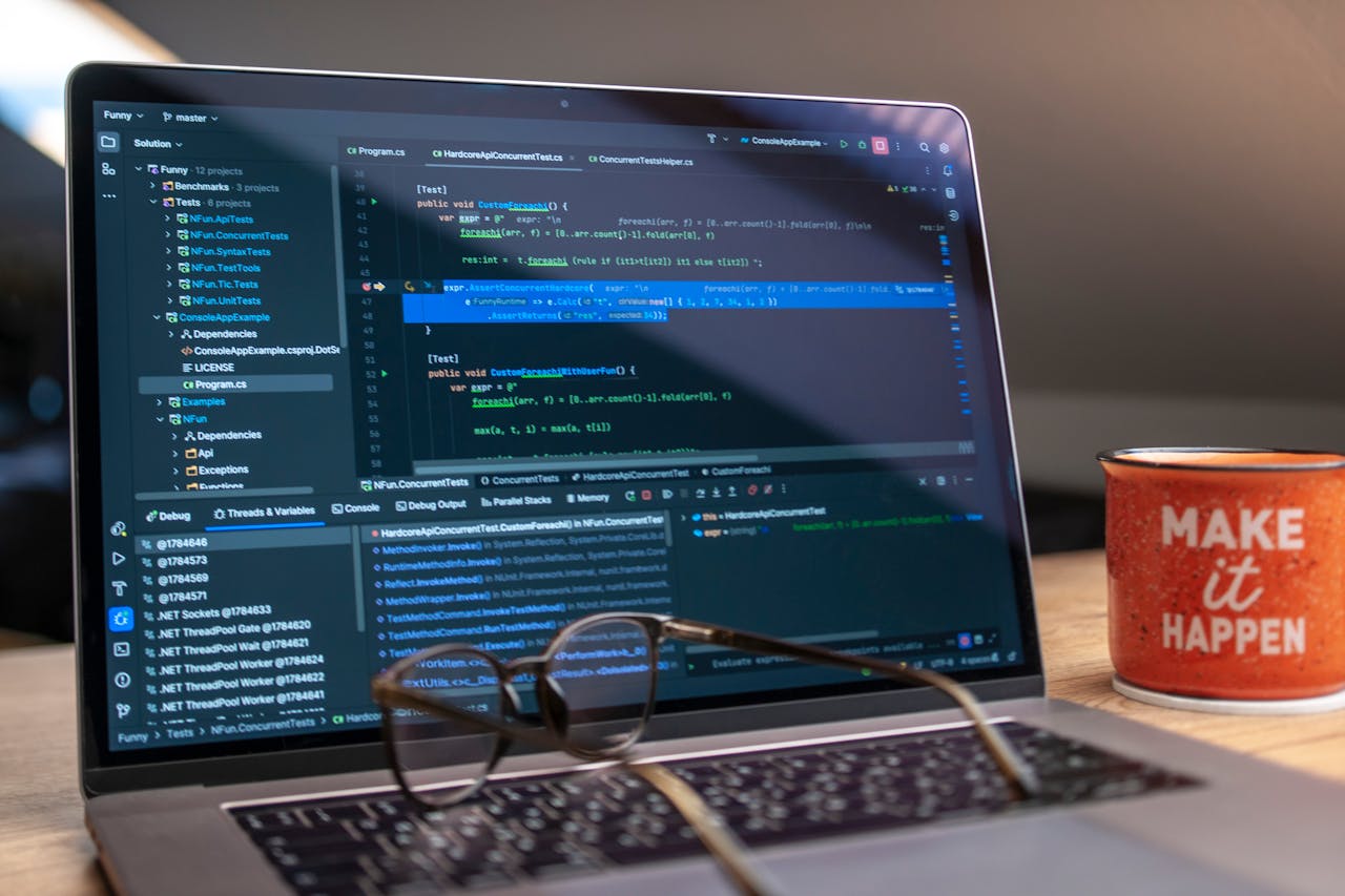 A laptop displaying code editor with a motivational mug that reads Make It Happen on a workspace.